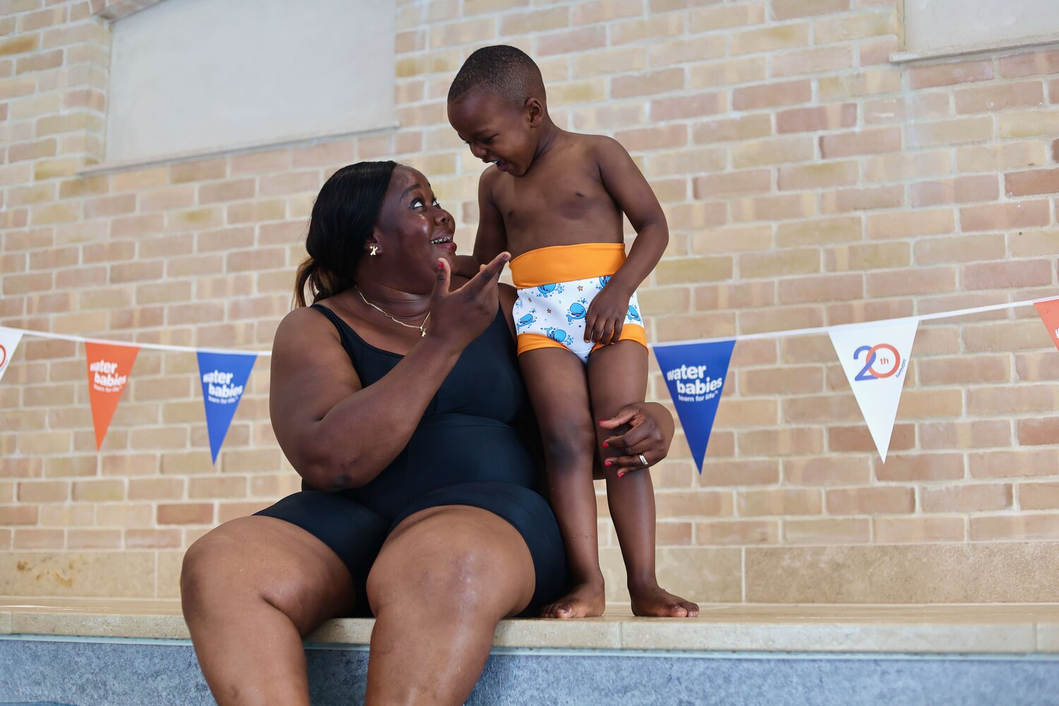 mum and toddler stood on pool side with water babies happy nappy on